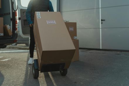 Delivery man with trolley unloading boxes from a van outside a warehouse.