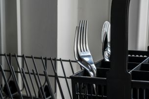 Close-up of stainless steel forks in a dishwasher rack, reflecting light and showcasing modern kitchenware.