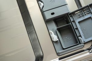 Closeup of an open dishwasher detergent compartment with water droplets visible.